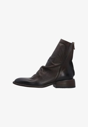 Bruine leren enkellaars met een slouch-ontwerp, zijrits en een lage gestapelde hak. Gladde textuur met subtiele glans en een gebogen tenen vorm.