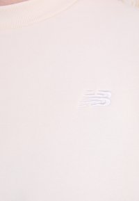 Sweatshirt beige clair avec un col côtelé et un logo blanc brodé sur la poitrine. Texture douce avec une coupe standard.