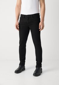 Jeans de mezclilla negra con un ajuste slim, que presentan un diseño clásico de cinco bolsillos. Combinados con botas de cuero negras hasta el tobillo y una camiseta blanca.