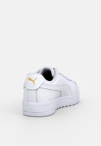 Baskets en cuir blanc à texture lisse, avec un logo doré sur le talon, une forme arrondie, et une semelle en caoutchouc blanche.