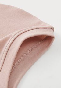 Hellrosa Baumwollstoff mit glatter Textur, ausgestattet mit einem abgerundeten, gesäumten Ausschnitt und dezenten Nähdetails.