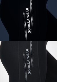 Zwarte sportlegging met een reflecterende "GORILLA WEAR" logo aan de zijkant, met verticale witte strepen en een gladde, rekbare textuur.