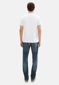 Camiseta blanca de manga corta con cuello redondo, combinada con jeans de mezclilla azul que tienen un corte recto y una textura desgastada, llevada con zapatos grises.