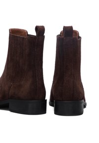 Bottines en daim marron avec une finition lisse, des panneaux latéraux élastiques et une semelle robuste en caoutchouc noir. Deux languettes sur la tige.