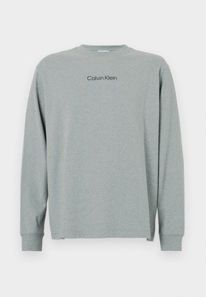 Tricou gri cu mânecă lungă, dintr-un material moale, cu guler rotund. Are un logo negru "Calvin Klein" pe piept și manșete ribbate. Design simplu.