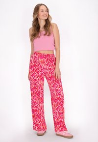 Roze geribbelde crop top gecombineerd met levendige, wijde broek in een kleurrijke dierenprint. Het model draagt zachte roze schoenen met een textuurgegeven zool.