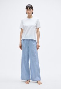 T-shirt blanc en coton à manches courtes, associé à un pantalon large à rayures verticales bleues, fabriqué en tissu léger.