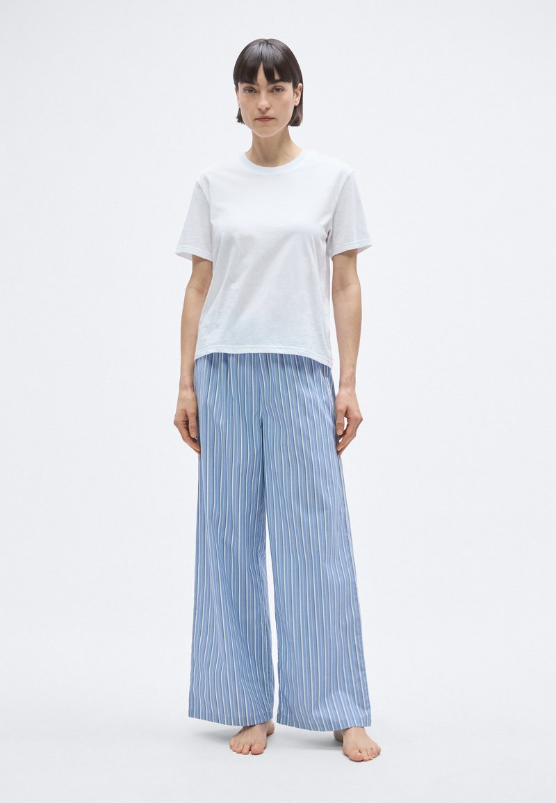 T-shirt blanc en coton à manches courtes, associé à un pantalon large à rayures verticales bleues, fabriqué en tissu léger.