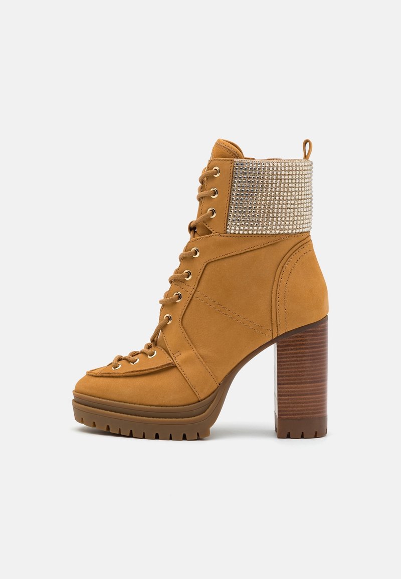 Bottine à talon haut beige avec laçage sur le devant, talon en bois épais, semelle crantée et détail de poignet orné de strass.