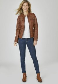 Bruine leren jas met een getailleerd ontwerp, met ritszakken, gecombineerd met een grijs T-shirt en donkerblauwe skinny jeans, afgewerkt met bruin enkellaarsjes.