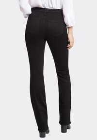 Sorte denimjeans med en tætsiddende talje og flagrende ben, med baglommer og en glat tekstur. Materialet ser ud til at være strækbart.