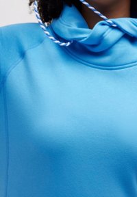 Sudadera azul claro con cuello alto y cordón, que presenta una textura suave y detalles de costura sutiles.