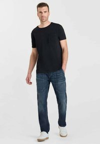 T-shirt nera a maniche corte con tasca anteriore, abbinata a jeans in denim blu sbiadito dotati di più tasche e completata da sneakers bianche.