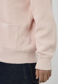 Pull en tricot rose clair avec texture côtelée, coupe oversize et poche avant. Caractérisé par des manches avec poignets côtelés et un détail de logo subtil.