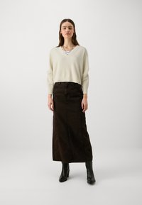 Krēmveida v-veida džemperis, garš brūns džinsu svārki un melnas potītes zābaki. Apģērbs ir ar brīvu piegriezumu un vienkāršu dizainu.