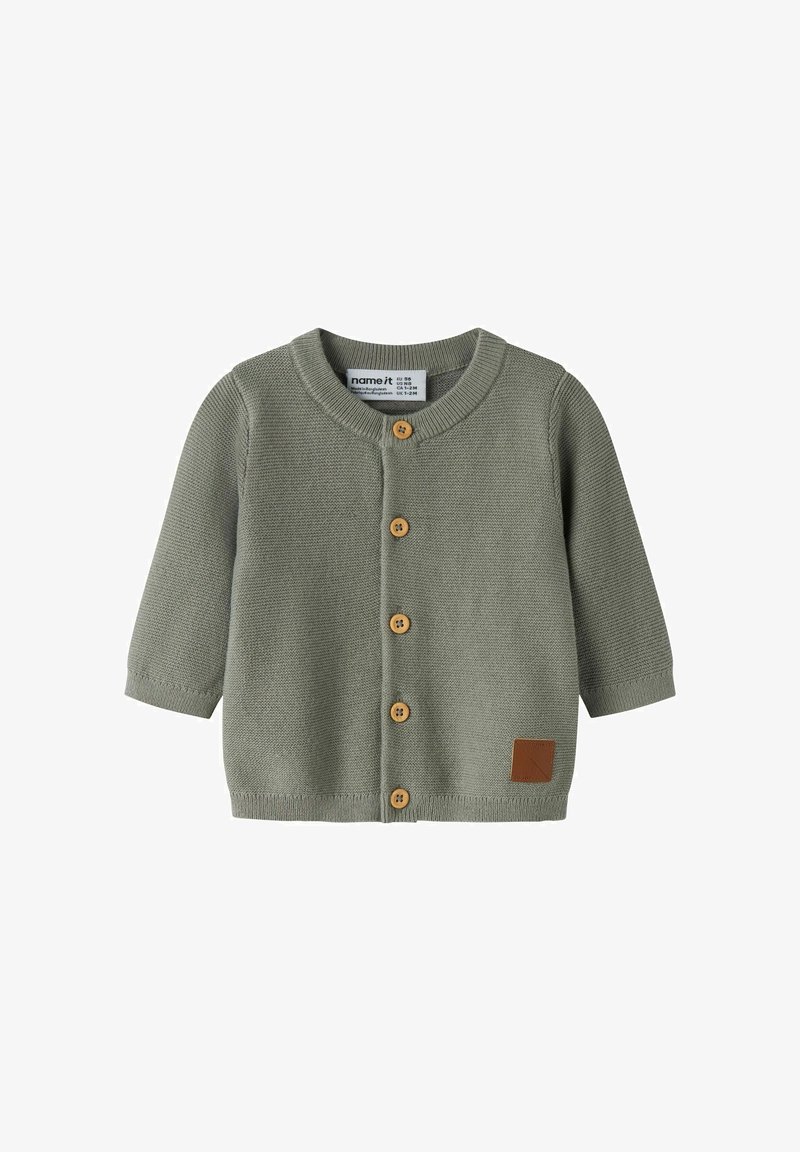 Cardigan bébé tricoté vert clair à manches longues, col rond, cinq boutons en bois sur le devant, et une petite écaille marron près de l'ourlet.