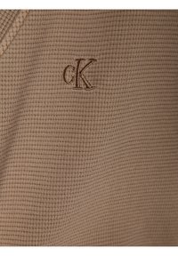 Béžová texturovaná látka s vaflovým pleteným vzorem, na přední straně s vyšívaným hnědým logem "cK".