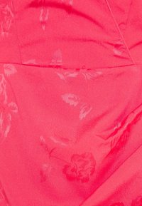 Tissu rose vif avec des motifs floraux subtils et des lignes de couture visibles, montrant de légères rides dans le matériau.