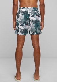 Shorts de bain pour homme en tissu blanc avec un imprimé de feuilles tropicales vertes. Taille élastique avec poches latérales. Coupe classique et longueur mi-cuisse.