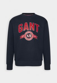 Sudadera de color azul marino con el texto en rojo "GANT" y el logotipo en negrita, cuello redondo acanalado y puños. Tejido suave con un corte holgado.
