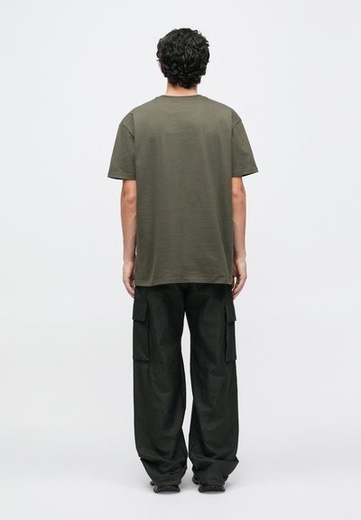 Olivnozeleni bombažni majica s kratkimi rokavi, sproščenega kroja in okroglo izrezom, v kombinaciji z ohlapnimi črnimi cargo hlačami z bočnimi žepi.