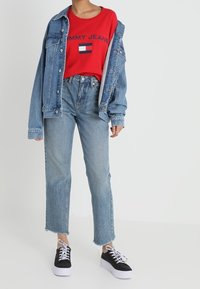 Camiseta roja de manga corta con el logo "TOMMY JEANS", chaqueta de denim, jeans rectos de color azul claro y zapatillas de plataforma negras con suelas blancas.
