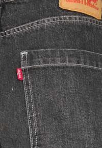 Gros plan sur la poche arrière d’un jean en denim foncé avec des coutures blanches et une étiquette rouge avec le logo Levi’s sur le côté.