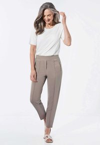 Helle beigen Hosen mit Seitentaschen, tailliertem Design und elastischem Bund, kombiniert mit einem schlichtweißen Kurzarmoberteil.