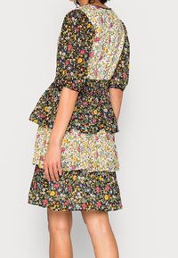 Schwarz-blumiges Kleid mit Puffärmeln, einem gerafften Bund und gestuftem Rock. Blumenmuster in mehreren Farben auf strukturiertem Stoff.