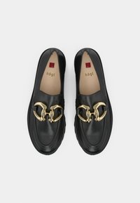 Een paar zwarte leren loafers met grote gouden kettingdetails en beige binnenzolen, gemarkeerd met "hōgl," vanuit bovenaf getoond op een witte achtergrond.