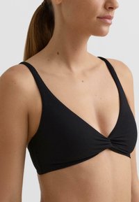 Črni rebrasti modrček z V-izrezom, z vrtinčasto podrobnostjo na sredini spredaj in tankimi naramnicami. Gladek tekstura, minimalen dizajn.