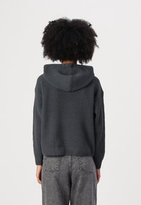 Donkergrijze gebreide hoodie met een gestructureerd oppervlak, voorzien van een capuchon en verlaagde schouders, gecombineerd met grijze high-waisted jeans.