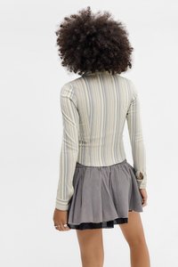Top cu mâneci lungi cu dungi în nuanțe de galben estompat și gri, design ajustat cu un guler înalt, asociat cu o fustă plisată gri cu accente negre.