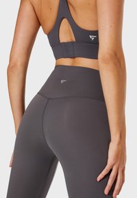 Reggiseno sportivo grigio con dettagli di taglio sulla schiena, abbinato a leggings grigi a vita alta con cuciture sottili e accento del logo.