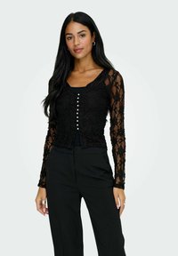 Sort blond lace top med lange ærmer og V-udsk�æring, med knaplukning foran med små hvide knapper og en cropped længde.
