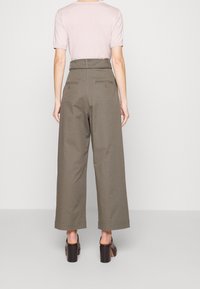 Pantalon olive à taille haute avec une coupe large, deux poches arrière et des coutures tailleur. Associé à une chemise ajustée rose clair.