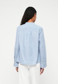 Lyseblå stribet skjorte med lange ærmer, krave og rygsplejsedetalje. Fremstillet af glat stof, med knapmanchetter og en afslappet pasform.