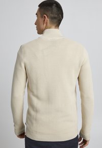 Beige geribde gebreide trui met een hoge kraag, lange mouwen en een snug fit. Textuurstof met een gladde afwerking.