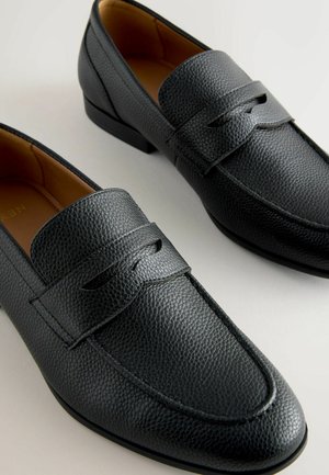 Zwarte leren instappers met een gestructureerde afwerking, voorzien van een decoratieve band over de wreef en een ronde neus. Platte rubberen zool.