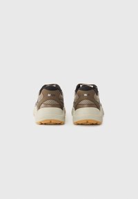Brown and beige athletic shoes with mesh upper, padded collar, and rubber sole. Features tonal accents and textured panels for breathability.