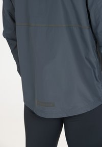 Herrarnas sportjacka i mörkblått, lättviktsmaterial med en slät yta. Har en reflekterande remsa och "ENDURANCE"-logotypen vid fållen.