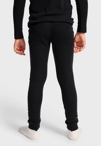 Svarta leggings med en sömlös design, med slim fit och mjuk textur, som smalnar av vid vristen. Vy från baksidan med ljusfärgade strumpor.