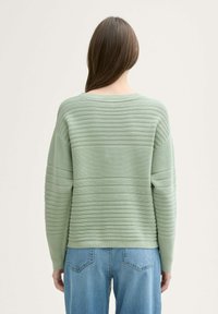 Suéter texturizado en verde menta con canalé vertical, cuello ancho y mangas largas, combinado con jeans de mezclilla azul claro.