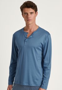 Langarm, blauwe henley-shirt gemaakt van zacht materiaal. Bevat drie knopen bij de kraag en heeft een comfortabele pasvorm.
