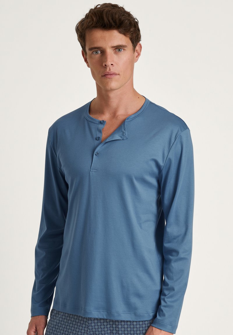 Langarm, blauwe henley-shirt gemaakt van zacht materiaal. Bevat drie knopen bij de kraag en heeft een comfortabele pasvorm.