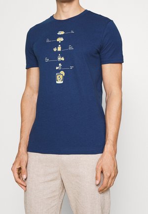 Muž v námořnicky modrém tričku s ilustrovaným receptem na margaritu, zobrazujícím kostky ledu, limetku, tequila, pomerančový likér, košer sůl a hotový nápoj.