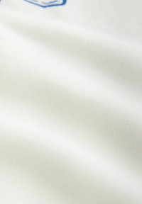 Tissu blanc à texture fine avec une vue partielle d'un emblème ou logo bleu et blanc sur le bord supérieur.