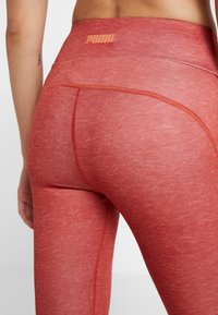 Leggings athlétiques rouges avec une texture lisse, une taille haute et des coutures contrastantes. Présente un logo Puma à l'arrière.