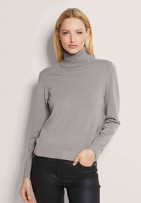 Grauer Rollkragenpullover aus weichem Stoff, mit langen Ärmeln und gerippten Bündchen und Saum. Getragen mit schwarzen Hosen, glatter Stoff sichtbar.