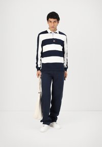 Marineblauw en witte gestreepte longsleeve polo met kraag, gecombineerd met marineblauwe broeken en witte sneakers. Draagt een canvas tote bag.